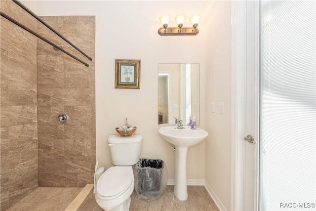 full bathroom featuring baseboards, a tile shower, and toilet