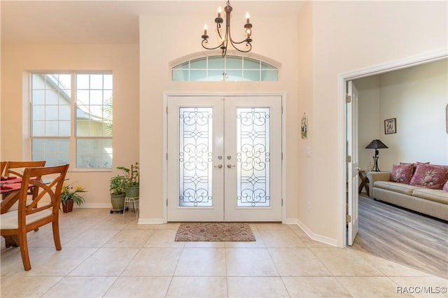 foyer entrance featuring a chandelier, french doors, light tile patterned floors, and baseboards