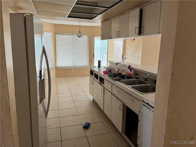 kitchen featuring pendant lighting, white appliances, sink, light tile patterned flooring, and white cabinetry