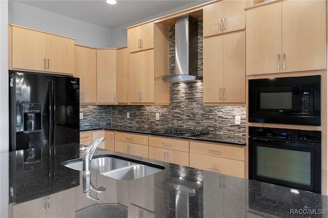 kitchen featuring dark stone countertops, wall chimney range hood, light brown cabinets, and black appliances