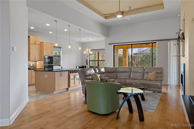 living room featuring a tray ceiling, ceiling fan with notable chandelier, and light hardwood / wood-style flooring