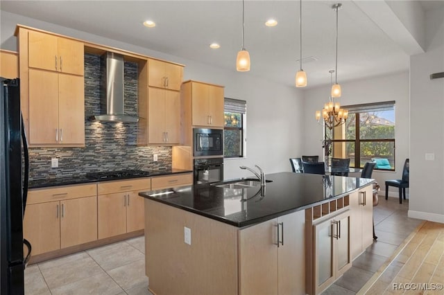 kitchen with sink, black appliances, a center island with sink, light brown cabinetry, and wall chimney exhaust hood