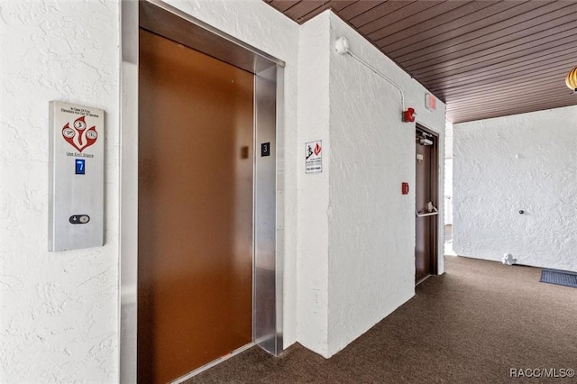 corridor featuring elevator, dark carpet, and wooden ceiling