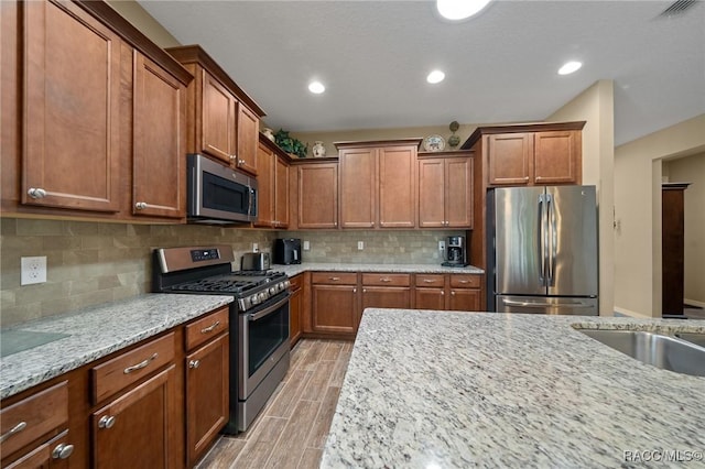 kitchen with light stone counters, appliances with stainless steel finishes, sink, and backsplash