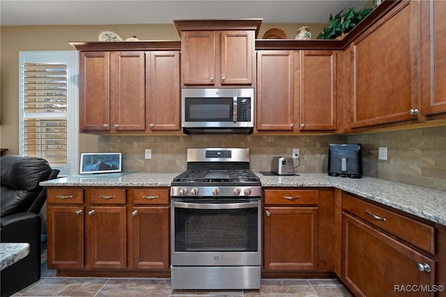 kitchen featuring stainless steel appliances, backsplash, and light stone counters