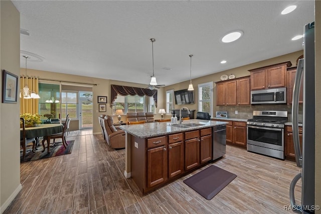 kitchen with sink, decorative light fixtures, appliances with stainless steel finishes, light stone countertops, and a kitchen island with sink