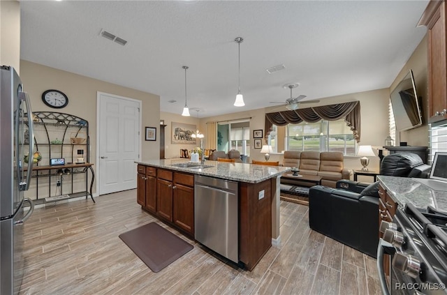 kitchen with pendant lighting, sink, appliances with stainless steel finishes, light stone countertops, and a center island with sink