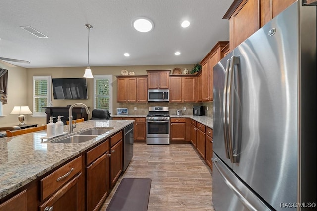 kitchen with appliances with stainless steel finishes, pendant lighting, tasteful backsplash, sink, and light stone countertops