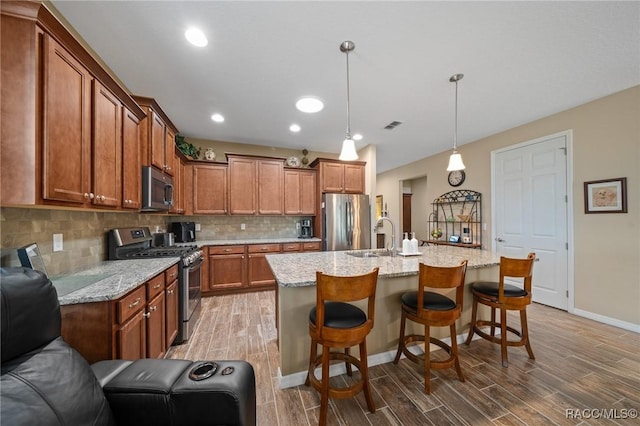 kitchen featuring pendant lighting, sink, a breakfast bar, stainless steel appliances, and an island with sink