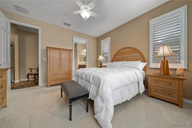 bedroom featuring light carpet, ensuite bath, and ceiling fan