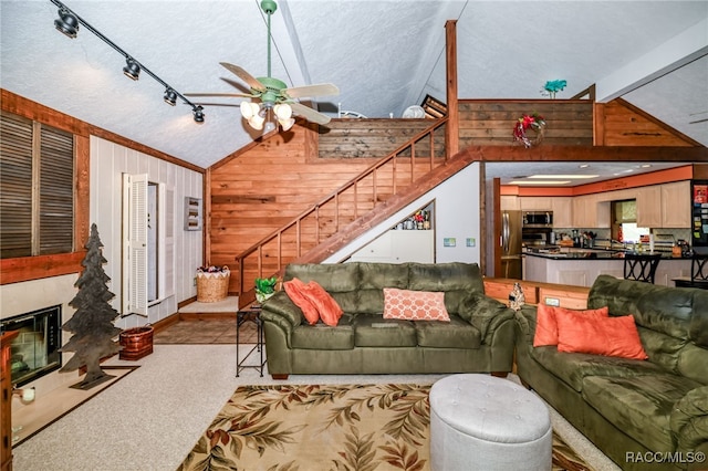 living room with carpet floors, lofted ceiling, stairway, a fireplace with flush hearth, and wooden walls