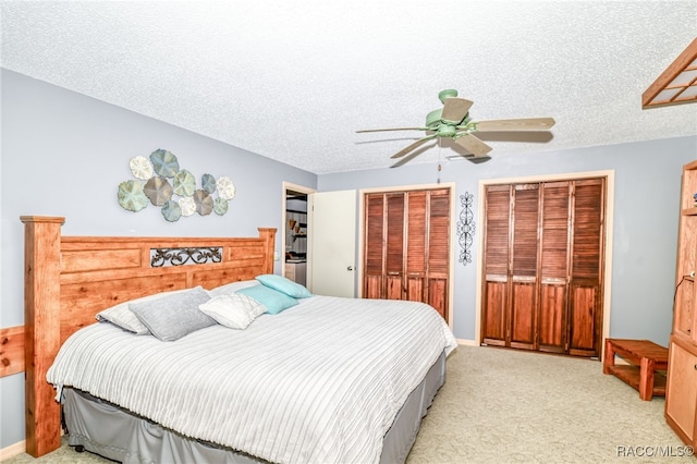 bedroom featuring baseboards, a ceiling fan, light colored carpet, a textured ceiling, and multiple closets