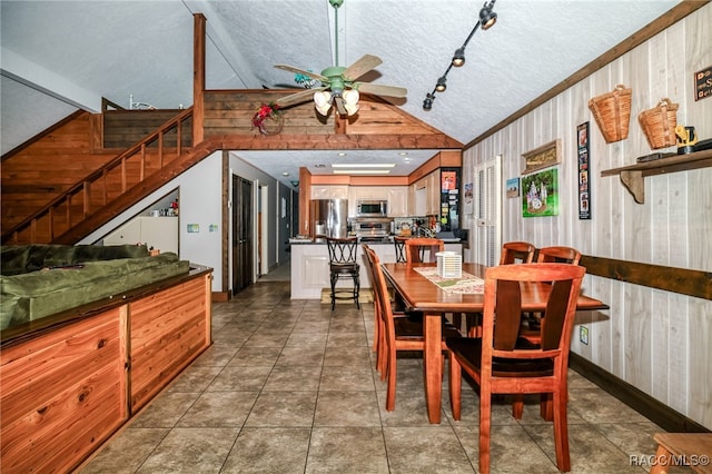 tiled dining space featuring a ceiling fan, vaulted ceiling, wooden walls, a textured ceiling, and stairs