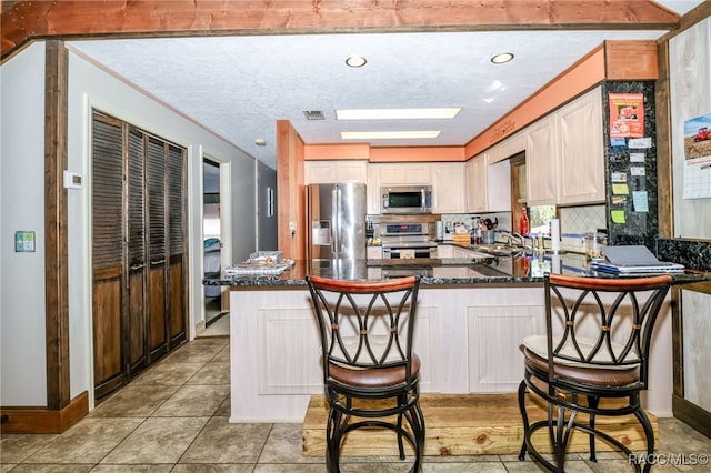 kitchen featuring stainless steel appliances, visible vents, decorative backsplash, dark stone countertops, and a peninsula