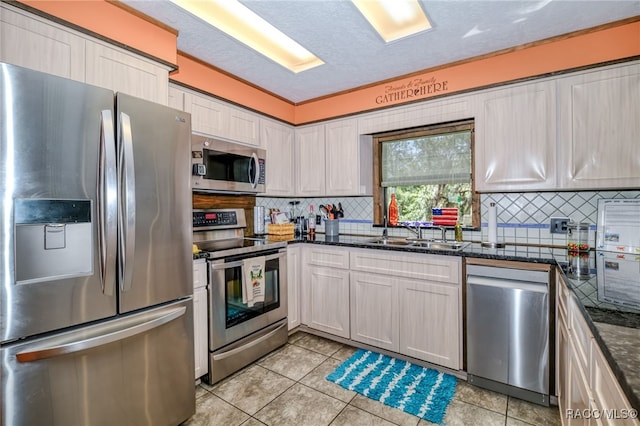 kitchen with light tile patterned floors, backsplash, appliances with stainless steel finishes, a sink, and dark stone counters