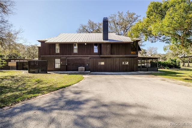 view of front facade with a chimney, aphalt driveway, metal roof, central air condition unit, and a front lawn