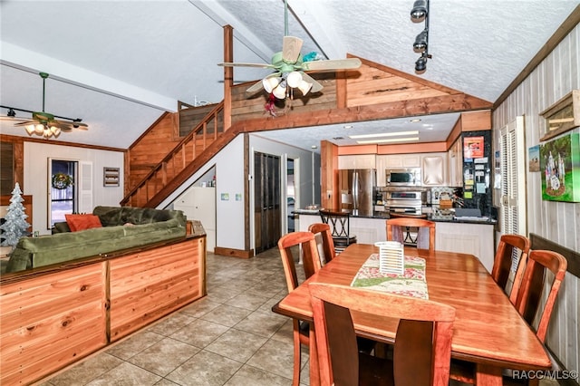 dining room featuring light tile patterned floors, wooden walls, ceiling fan, vaulted ceiling, and a textured ceiling