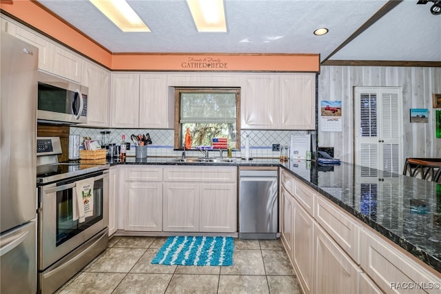 kitchen featuring light tile patterned flooring, a sink, appliances with stainless steel finishes, decorative backsplash, and dark stone counters