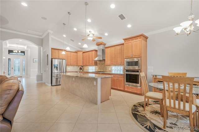 kitchen with a center island with sink, appliances with stainless steel finishes, light stone counters, wall chimney range hood, and backsplash