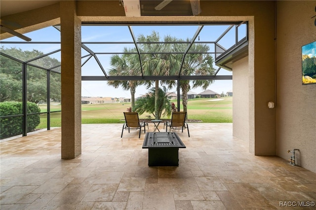 view of patio featuring ceiling fan, glass enclosure, and a fire pit