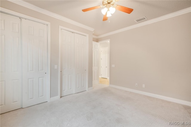 unfurnished bedroom with light carpet, two closets, ceiling fan, and crown molding