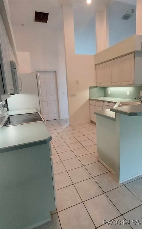 kitchen featuring stove, a high ceiling, visible vents, light tile patterned floors, and a peninsula