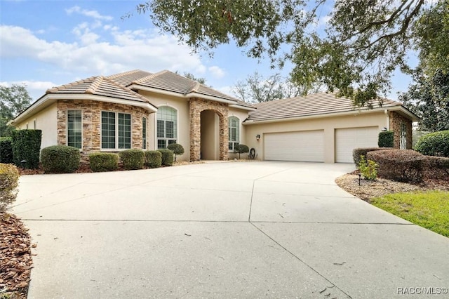 view of front of home with driveway, an attached garage, stucco siding, stone siding, and a tiled roof