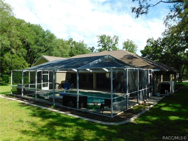 back of house featuring glass enclosure and a yard