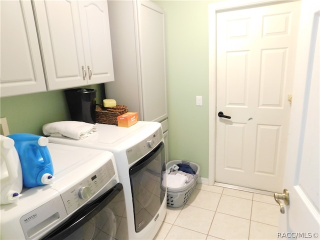 clothes washing area with washer and clothes dryer, light tile patterned floors, and cabinets