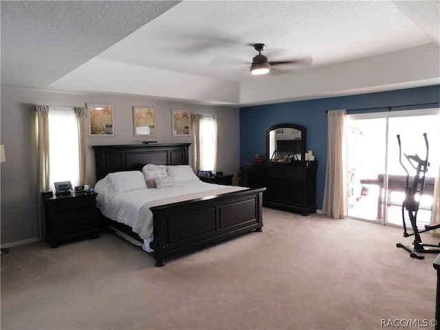 carpeted bedroom featuring ceiling fan, a raised ceiling, a textured ceiling, and multiple windows