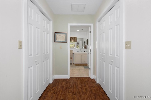 hallway with dark wood-type flooring, visible vents, a sink, and baseboards