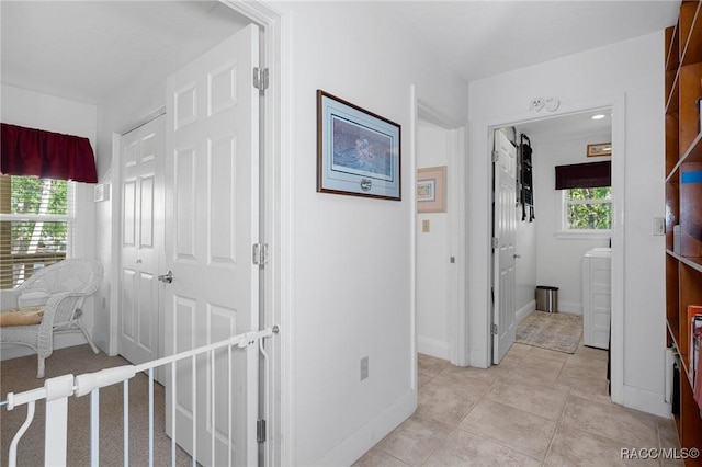 hall featuring baseboards, washer / clothes dryer, and light tile patterned flooring