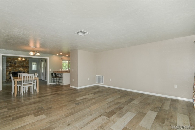 unfurnished living room featuring a stone fireplace, wood-type flooring, a textured ceiling, and an inviting chandelier