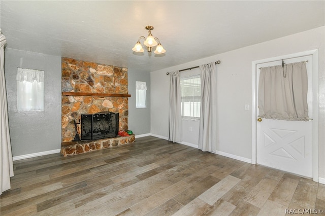 unfurnished living room with a chandelier, hardwood / wood-style flooring, and a stone fireplace