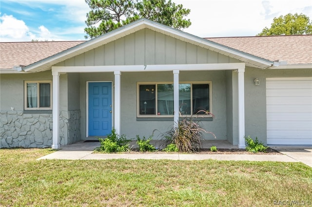 view of exterior entry featuring covered porch, a garage, and a lawn