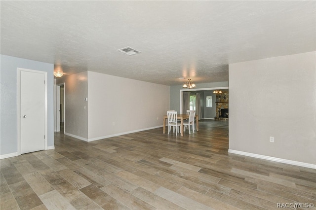 unfurnished room with hardwood / wood-style floors, a textured ceiling, a stone fireplace, and a notable chandelier