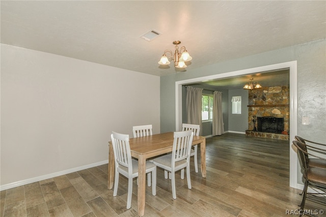 dining room featuring dark hardwood / wood-style floors, a stone fireplace, and a chandelier