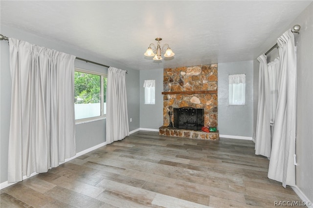 unfurnished living room featuring a chandelier, wood-type flooring, and a stone fireplace