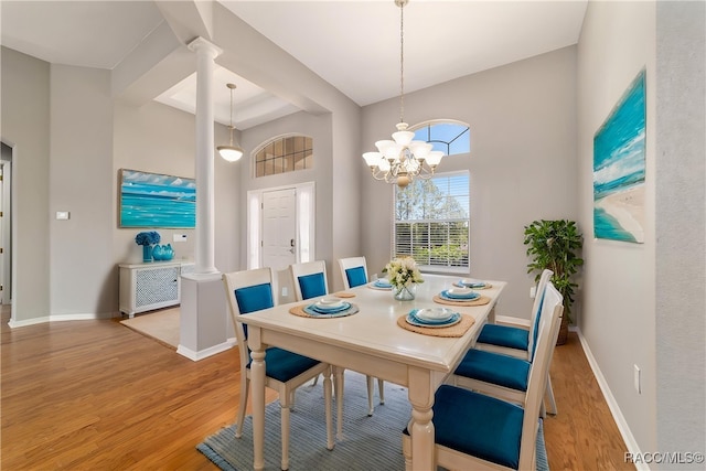 dining area featuring light wood-type flooring, a high ceiling, baseboards, a chandelier, and decorative columns