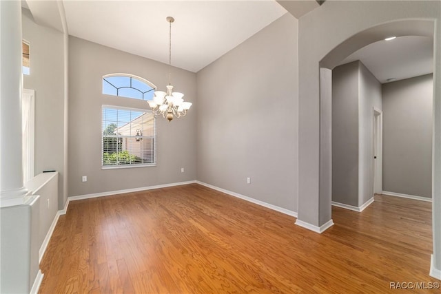 unfurnished room with arched walkways, baseboards, a chandelier, and wood finished floors