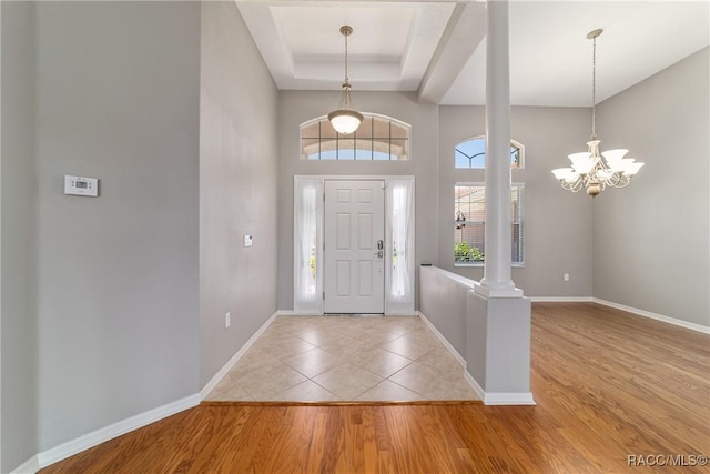 foyer entrance featuring ornate columns, a tray ceiling, a notable chandelier, light wood-type flooring, and baseboards