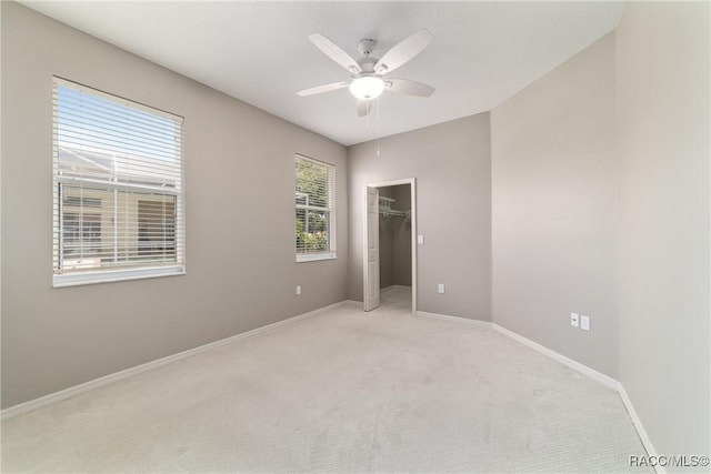 unfurnished bedroom featuring light colored carpet, baseboards, a walk in closet, and ceiling fan