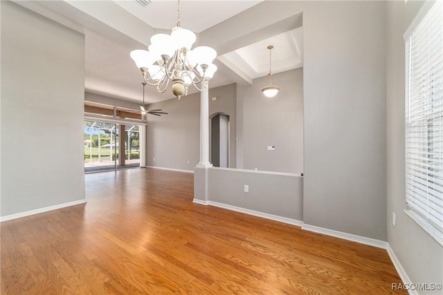 spare room with ceiling fan with notable chandelier, wood finished floors, beam ceiling, arched walkways, and baseboards