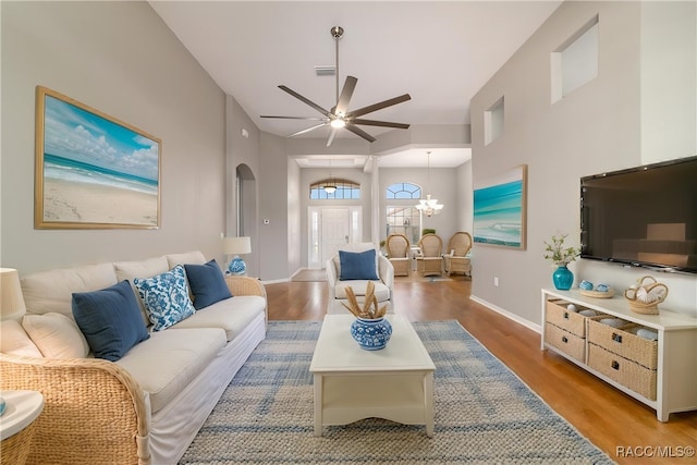 living room featuring a ceiling fan, wood finished floors, a chandelier, arched walkways, and baseboards