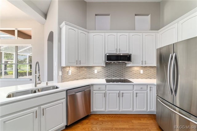 kitchen with backsplash, stainless steel appliances, white cabinetry, and a sink