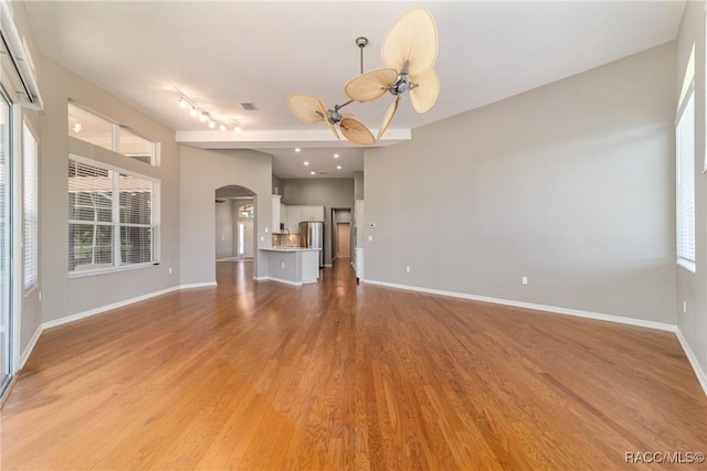 unfurnished living room with light wood-style flooring, a wealth of natural light, arched walkways, and a ceiling fan