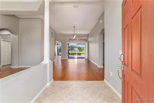 foyer entrance with visible vents, ceiling fan, arched walkways, light tile patterned floors, and baseboards