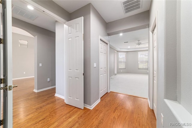 corridor featuring light wood finished floors, arched walkways, and baseboards