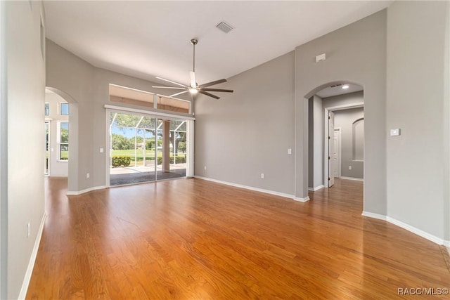 spare room with arched walkways, a ceiling fan, wood finished floors, and baseboards