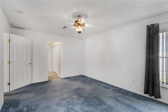 spare room with a textured ceiling and dark colored carpet